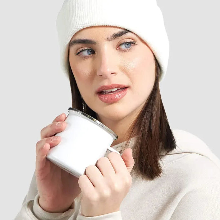 Woman wearing a white beanie and holding a white mug against a light gray background