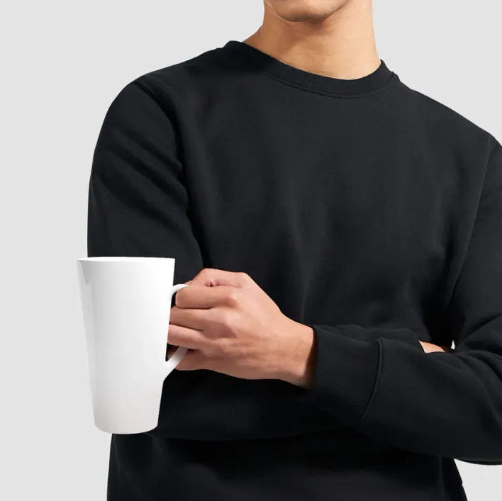 Person wearing a black sweatshirt holding a white mug against a light gray background